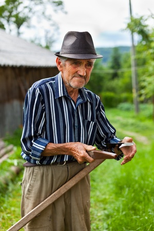 Senior farmer sharpening his scythe to mow the lawn traditionallyの写真素材