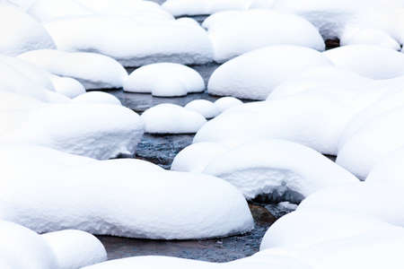 Creek flowing among boulders covered in snowの写真素材