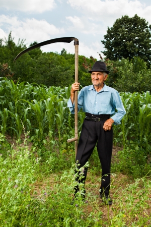 Senior farmer with scythe near a corn field having a break from workの写真素材