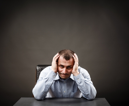 Depressed businessman or white collar worker at his desk holding his headの写真素材