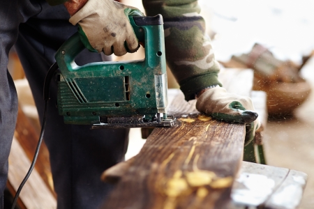 Man with protection gloves using an electric saw to cut a plankの写真素材