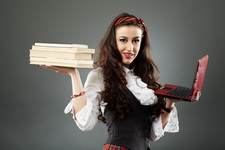 Young teenager in school uniform, presenting some books in one hand and a laptop in the other, in closeup pose, isolated on gray backgroundの写真素材