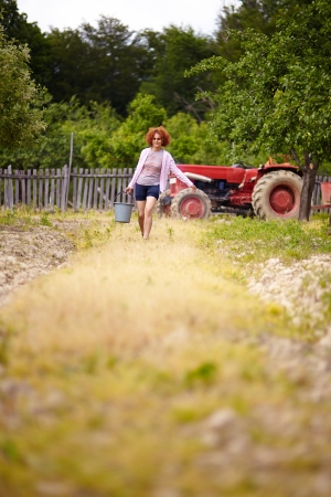 Farmer woman carrying a bucket with fertilizer in an orchard, with selective focusの写真素材
