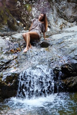 Sexy young woman laying on the mountain rock near a waterfallの写真素材