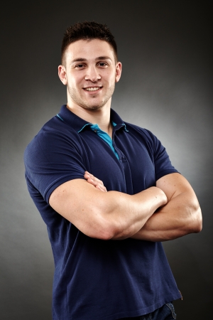 Studio shot of handsome young man wearing a navy blue polo t-shirt with arms foldedの写真素材