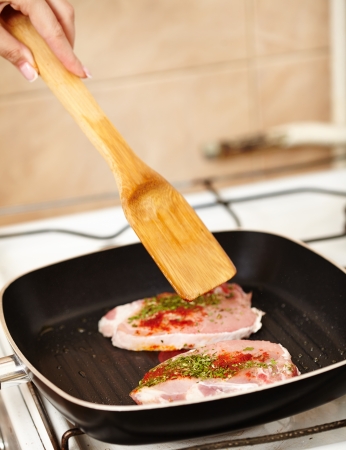 Closeup of cook's hand preparing a spiced pork chop steak in the frying pan on the stoveの写真素材