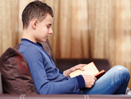 Teenage caucasian boy reading a book on the sofa, selective focusの写真素材