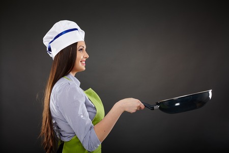 Studio shot of a young woman cook holding a wok pan over gray backgroundの写真素材