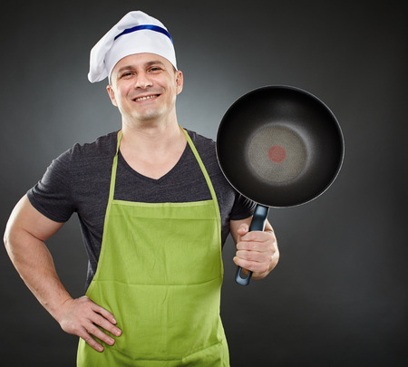 Caucasian chef in apron and hat, with wok pan over gray backgroundの写真素材