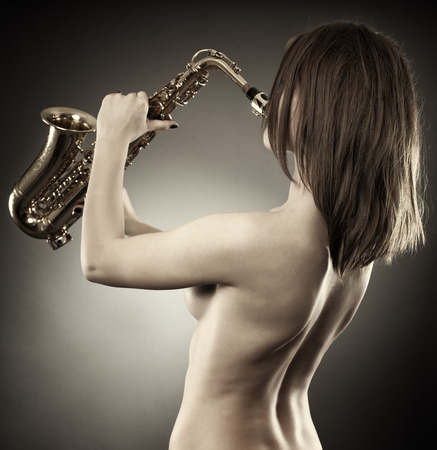 Back of a topless young woman playing the saxophone, monochrome toned imageの写真素材