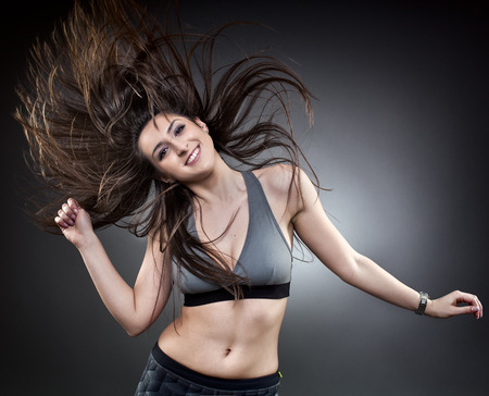 Young woman dancing with her long hair fluttering in motion, studio shot on grayの写真素材