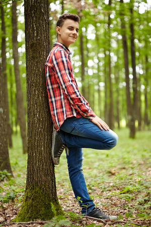 Trendy and handsome teenage boy in plaid shirt, outdoor in a forestの写真素材