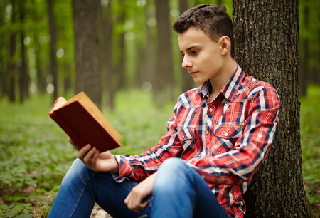 Candid shot of a teen boy reading a book in the forestの写真素材