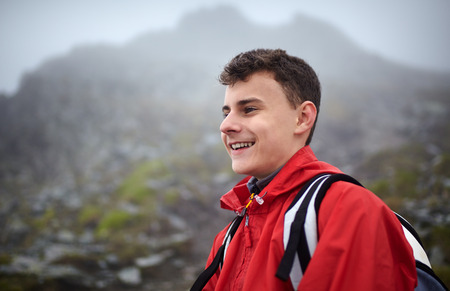 Teenage boy hiker in rain coat resting after hiking on mountain trail