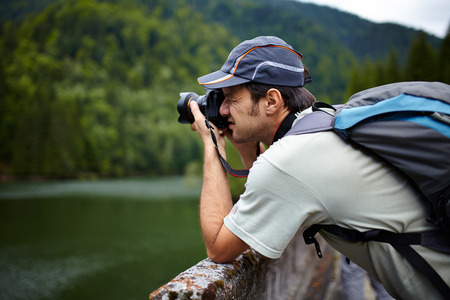 Closeup of a tourist taking photos of a lake in the mountains