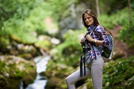 Young woman hiker with backpack crossing a river among boulders covered with moss in a canyonの写真素材