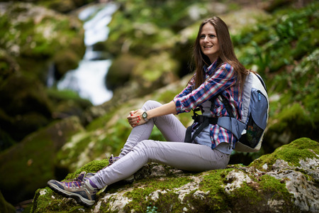 Young woman hiker with backpack resting on moss covered rocks in a canyonの写真素材