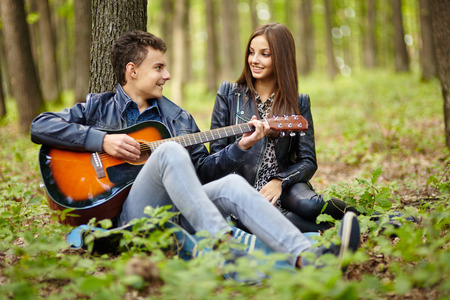 Teenager playing guitar for his girlfriend outdoor in the forest