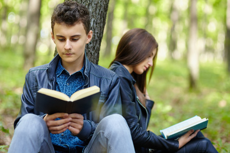 Teenagers students boy and girl reading outdoor in a forest
