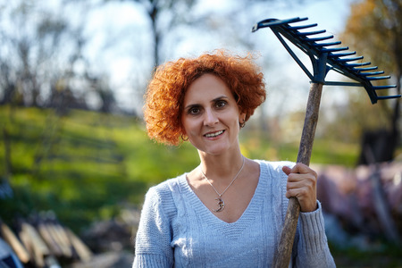 Caucasian farmer woman with a rake cleaning her garden of fallen leavesの写真素材