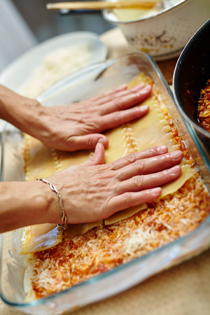 Woman cooking lasagna, arranging the pasta in a tray with fillingの写真素材