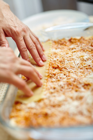 Woman cooking lasagna, arranging the pasta in a tray with fillingの写真素材