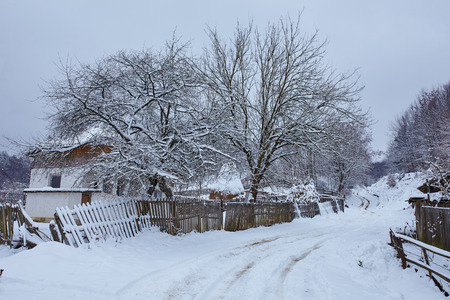 Landscape with snow-covered country road and old house in a villageの写真素材