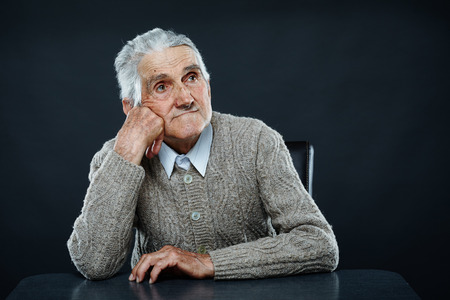 Happy 80 years old man sitting at the desk, studio shotの写真素材