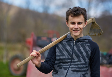 Closeup portrait of a smiling teenager boy holding a hoe outdoorの写真素材