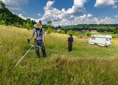 Young farmer mowing the lawn with a trimmer