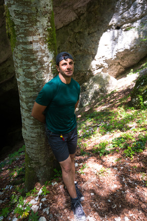 Mature caucasian man leaning against a tree near the entrance of a caveの写真素材