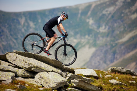 Mountain bike cyclist in sport equipment and helmet riding on rugged trailsの写真素材