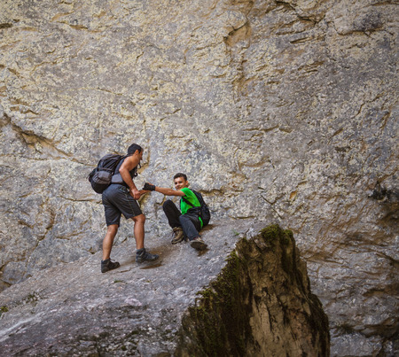 Caucasian hiker helping teenage boy to get up on a huge mountain cliffの写真素材