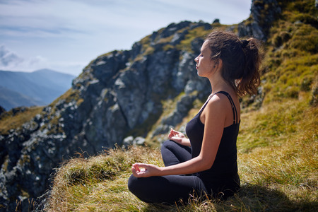 Young beautiful woman yoga meditating  and relaxing on the top of a mountain at sunriseの写真素材