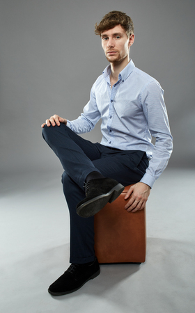 Caucasian young businessman sitting on a chair in a studio, over gray backgroundの写真素材