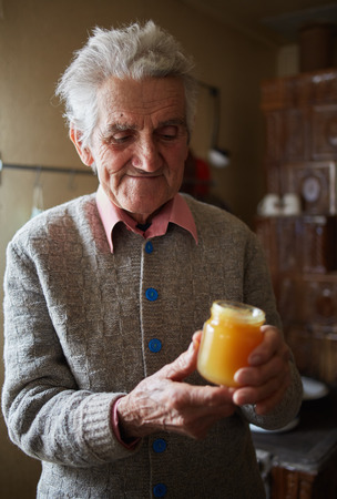 Old man indoor holding happy a jar of honey with pollenの写真素材