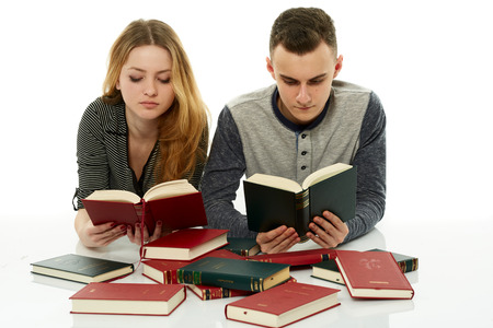Teenage students doing homework together, with many books around themの写真素材