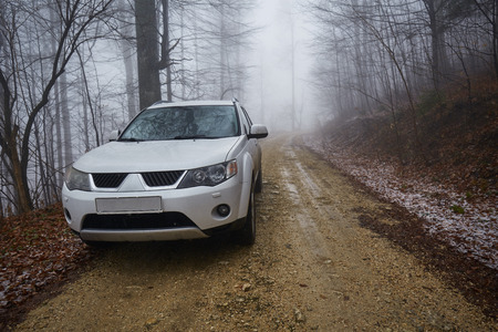 White SUV car on an offroad trail in a foggy day