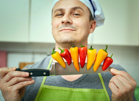 Chef holding many peppers on the edge of his knifeの写真素材