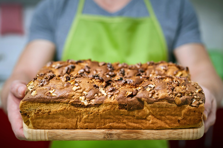 Happy cook holding a board with a cake with walnuts freshly out of the ovenの写真素材