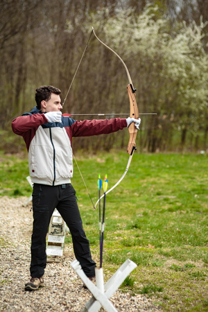 Teenage boy shooting with a bow in an open air range