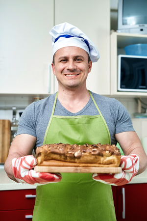 Happy cook holding a board with a cake with walnuts freshly out of the ovenの写真素材