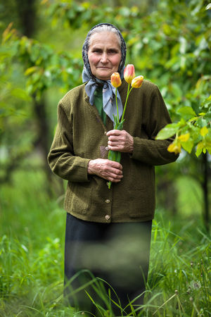Happy old woman with flowers outdoor in the gardenの写真素材