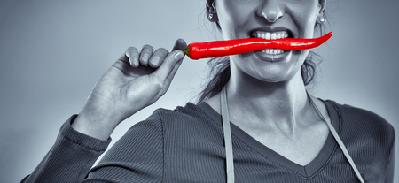 Attractive woman cook biting a hot chili pepperの写真素材