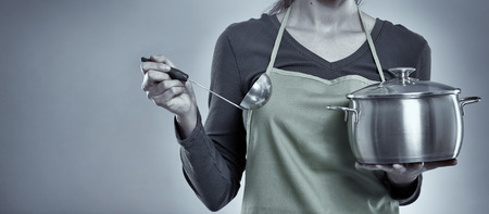 Woman cook smiling and holding a pot over gray backgroundの写真素材