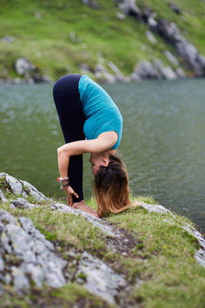 Young woman practicing yoga by a lake in the mountainsの写真素材