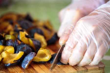 Woman's hands slicing plums on a wooden board to make jam or chutneyの写真素材