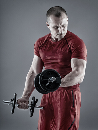Fitness man doing biceps curl with dumbbells on gray backgroundの写真素材