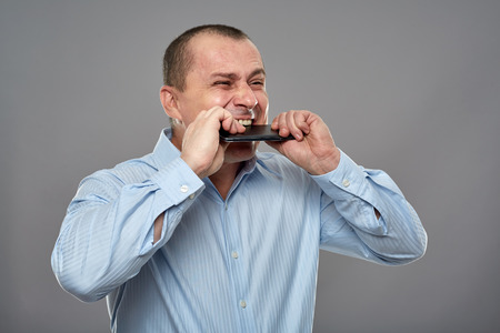 Angry business man biting his cellphone on gray background