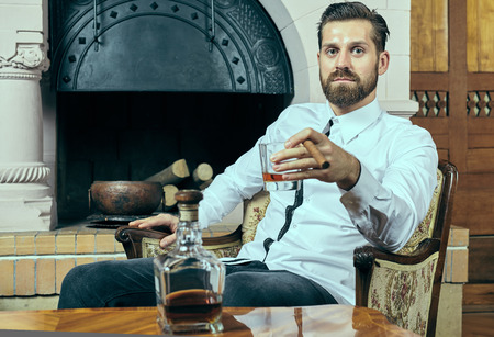 Young man with beard having a glass of scotch and a cigarの写真素材